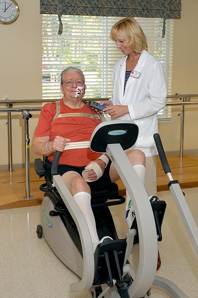 A resident using a fitness machine with staff assistance