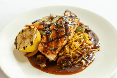 A plate of grilled salmon with vegetables and noodles