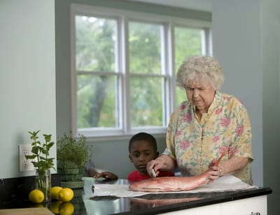 An elderly woman preparing fish with a child in a kitchen