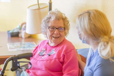 A senior resident laughing with a staff member indoors