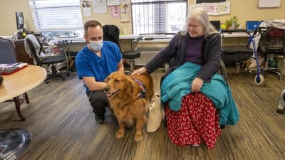 Staff member with a resident and a therapy dog in an activity room