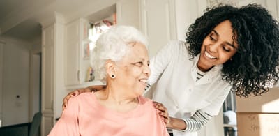A caregiver smiling while assisting a senior woman.