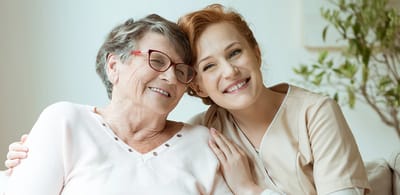 A caregiver and resident smiling together indoors.