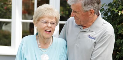A caregiver and a resident share a joyful moment outdoors.