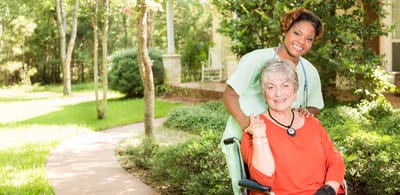 Nurse assisting elderly woman in a garden setting.