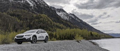Vehicle parked by a river with mountains in the background.