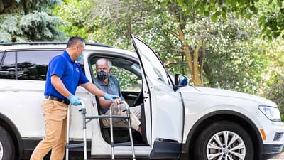Caregiver assisting senior into a vehicle outdoors.
