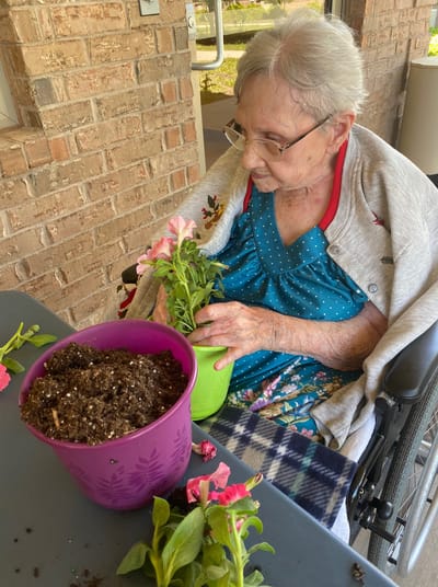 Senior woman planting flowers in a colorful pot.