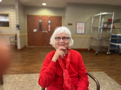 Senior resident in a cheerful red outfit in common area.
