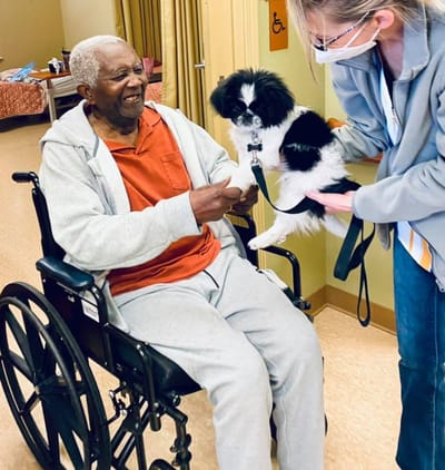 Resident enjoying time with a dog in a wheelchair.