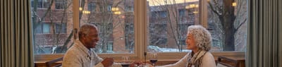 Two seniors enjoying a meal together by a large window.