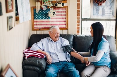 A caregiver checking a senior man's blood pressure in a cozy room