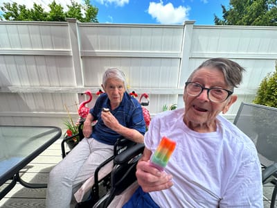 Two seniors enjoying popsicles on a patio.