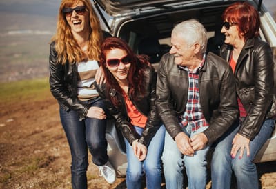 Group of four people laughing outdoors by a car.
