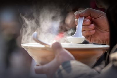 A hand holding a bowl of steaming soup
