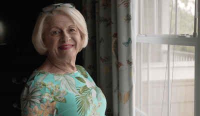 Smiling woman by a window with floral curtains.
