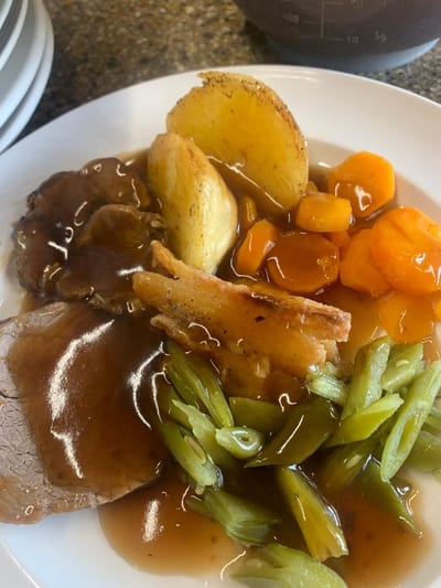 A plate of food with roast, vegetables, and sauce.