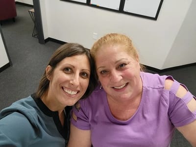 Two women smiling together in an indoor setting.