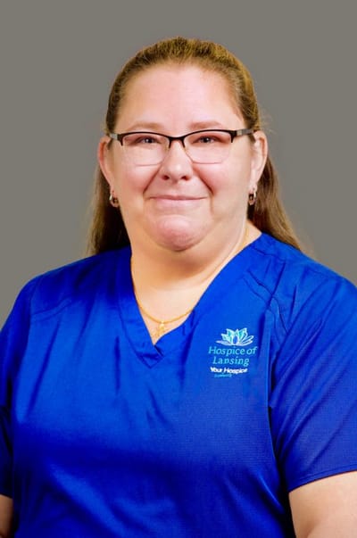 Staff member in blue scrubs smiling at the camera.