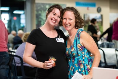 Two staff members smiling together in a social setting.