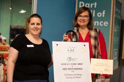 Two staff members presenting food items at an event.