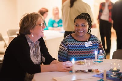 Two women smiling and talking at a table.