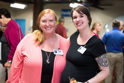 Two staff members smiling with drinks at an event.