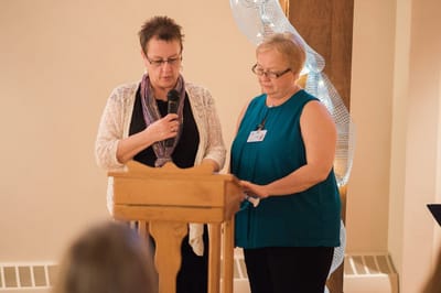 Two women speaking at a podium in a community event.