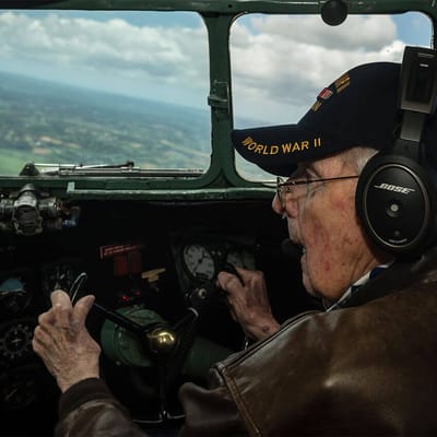 An elderly man wearing a WWII cap in a cockpit