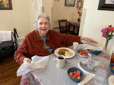 A smiling resident enjoying a meal in the dining room.