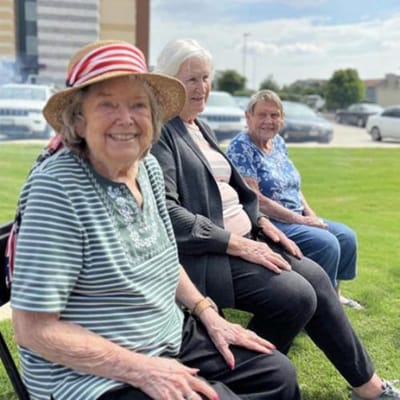 Three smiling residents sitting outside on a sunny day