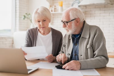 Seniors reviewing documents at a table with a laptop