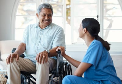 Fairhaven Healthcare Center for Rehabilitation and Nursing, Nursing Home in Lowell, MA — Smiling senior man in wheelchair with attentive caregiver