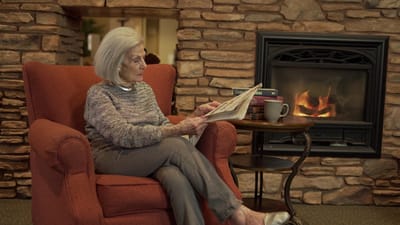 Resident reading in a cozy common area by the fireplace