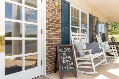 Exterior of Manning Place with rocking chairs and welcome sign