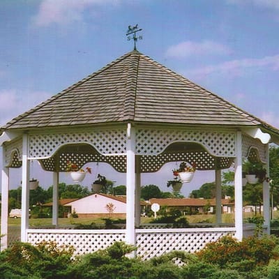 A gazebo with hanging flower pots in a green space