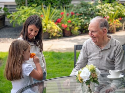 An elderly man enjoying time with two young girls in a garden