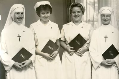 Four staff members in nursing attire holding documents