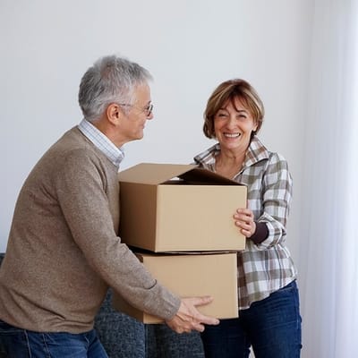 Two residents smiling while carrying boxes in a spacious room
