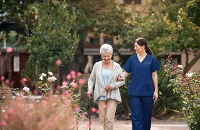 A staff member walks with a resident in a garden