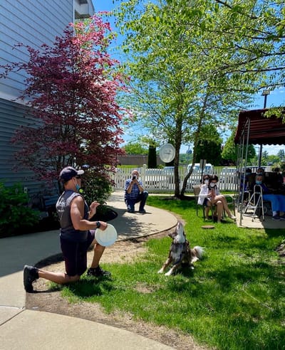 The Inn at Fairview, nursing home in Hudson, NH — Man playing frisbee with a dog in a courtyard