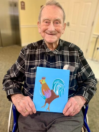 The Inn at Fairview, nursing home in Hudson, NH — Elderly man holding a colorful rooster painting