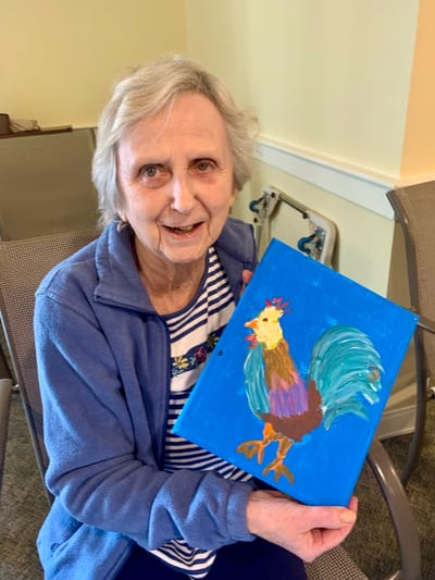 The Inn at Fairview, nursing home in Hudson, NH — Elderly resident displaying a colorful rooster painting