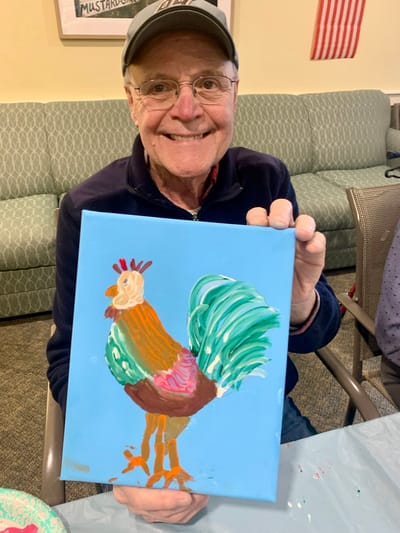 The Inn at Fairview, nursing home in Hudson, NH — Senior resident proudly displaying a colorful rooster painting