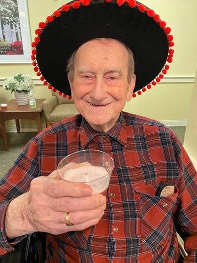 The Inn at Fairview, nursing home in Hudson, NH — Smiling resident wearing a festive hat holding a drink