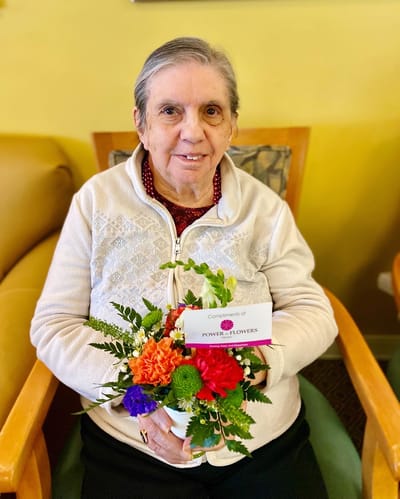 The Inn at Fairview, nursing home in Hudson, NH — Elderly woman holding a floral arrangement in a lounge