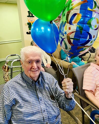 The Inn at Fairview, nursing home in Hudson, NH — Elderly man holding colorful balloons in a common area