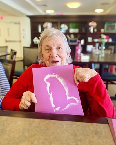The Inn at Fairview, nursing home in Hudson, NH — Senior resident holding artwork in a communal setting