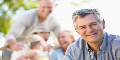 A man smiling outdoors with family behind him