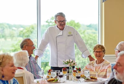 Residents enjoying a meal with a chef in a dining room
